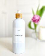 Refillable shampoo bottle in white with bamboo pump for minimalist bathroom.