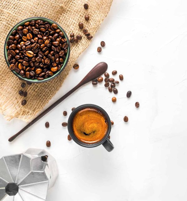 Tasse à café avec expresso fort avec mousse, une cafetière et des grains de café dans un bol sur fond de béton blanc. Vue de dessus avec espace de copie.